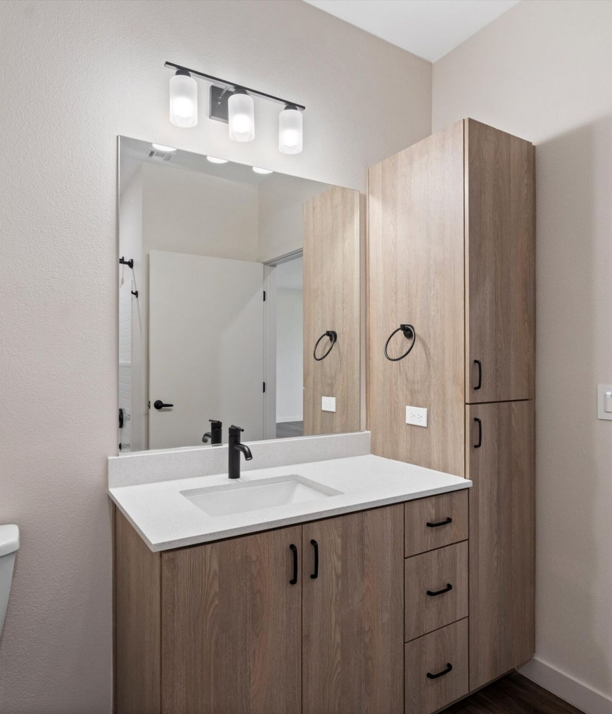 Modern bathroom with a wood vanity, large mirror, white sink, black faucet, and toilet next to the counter.