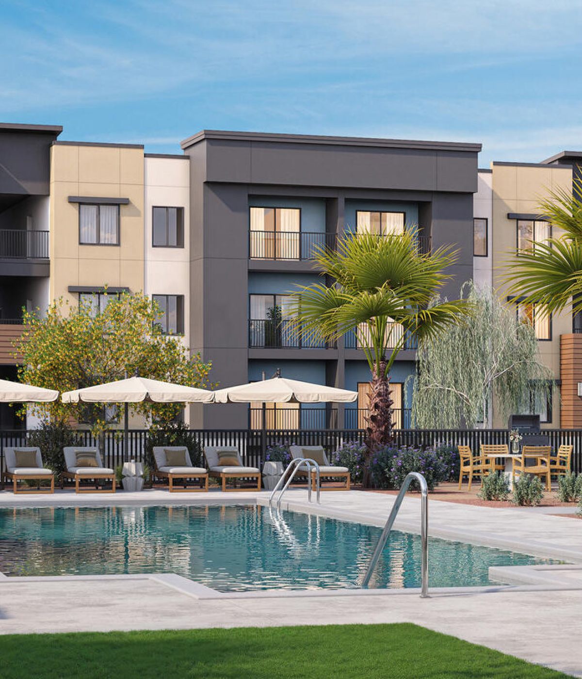 Modern apartment complex with a swimming pool, lounge chairs, umbrellas, and palm trees under a blue sky.